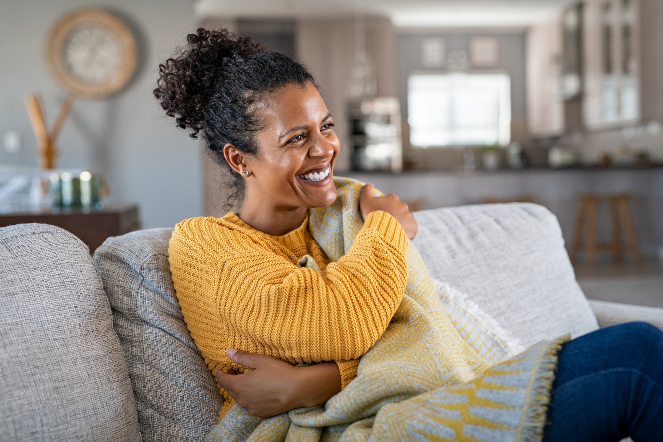 Woman with blanket on couch laughing